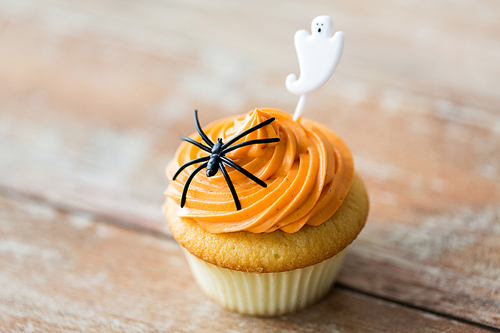 food, baking and holidays concept - cupcake or muffin with halloween party decorations on wooden table