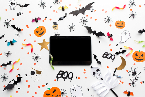 holidays, technology and party concept - halloween decorations and candies with tablet pc computer over white background