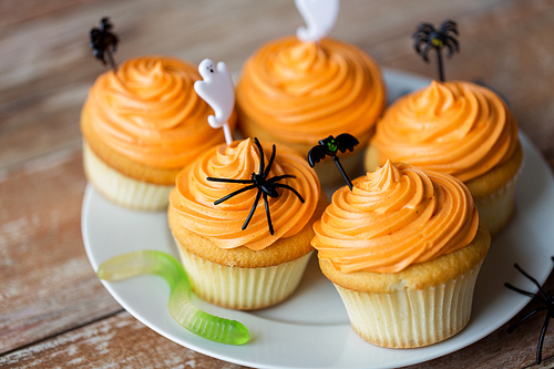 food, baking and holidays concept - cupcakes or muffins with halloween party decorations and candies on plate