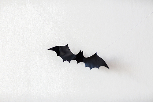 halloween, decoration and scary concept - black bat hanging on strings over white background