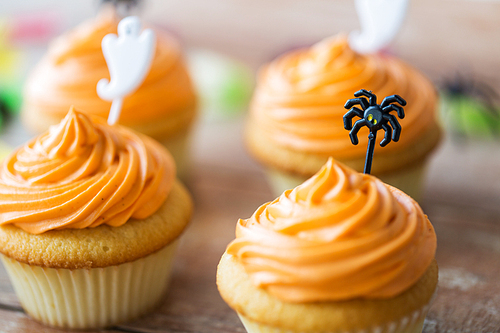 food, baking and holidays concept - cupcakes or muffins with halloween party decorations on wooden table