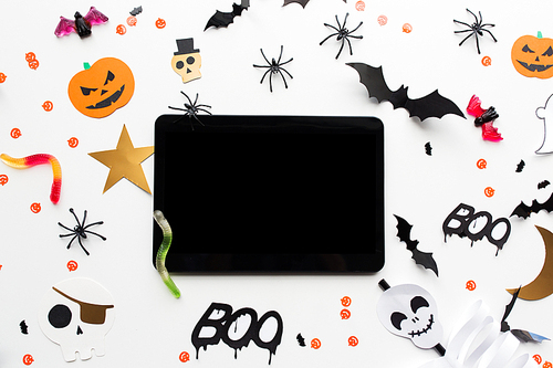 holidays, technology and party concept - halloween decorations and candies with tablet pc computer over white background