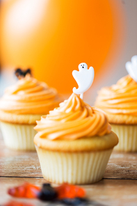 food, baking and holidays concept - cupcake or muffin with halloween party ghost decoration on wooden table