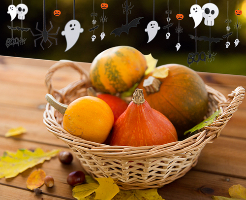 halloween and holidays - pumpkins in wicker basket with leaves on wooden table and paper party decorations over dark background