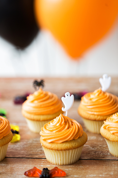 food, baking and holidays concept - cupcakes or muffins with halloween party ghost decoration on wooden table