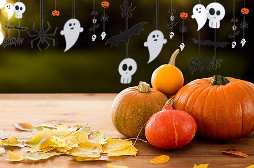 halloween and holidays - pumpkins with autumn leaves on wooden table and paper party decorations over dark background