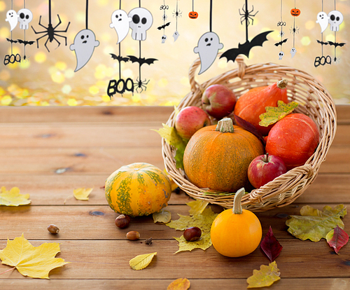 halloween and holidays - pumpkins in wicker basket with leaves on wooden table and paper party decorations over festive lights background