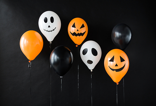 holidays, decoration and party concept - air balloons with funny and evil faces for halloween on black background