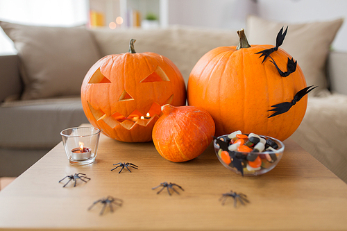 holidays, decoration and party concept - jack-o-lantern or carved pumpkin with halloween decorations and treats on wooden table at home room