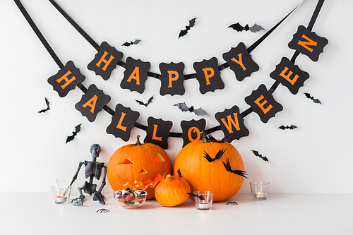 halloween, holidays and decoration concept - jack-o-lantern or carved pumpkins with candies and festive garland on white background