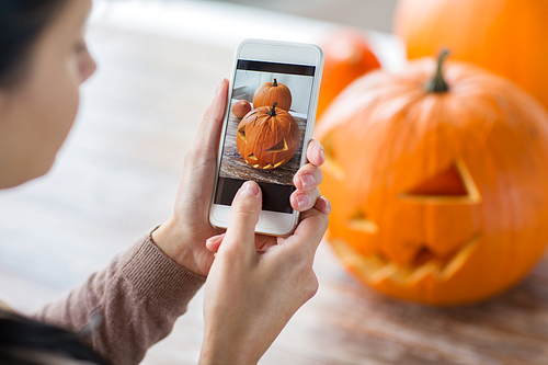 halloween, decoration and holidays concept - close up of jack-o-lantern or carved pumpkin and hands with smartphone