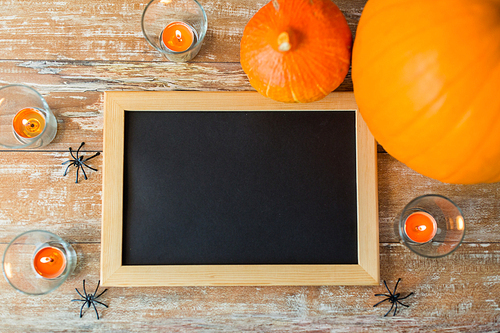 holidays, school and party concept - halloween pumpkins, decorations with blank chalkboard on wooden boards background