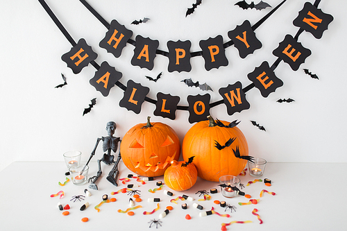 halloween, holidays and decoration concept - jack-o-lantern or carved pumpkins with candies and festive garland on white background