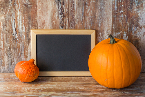 holidays, school and  concept - pumpkins with blank chalkboard on wooden boards background