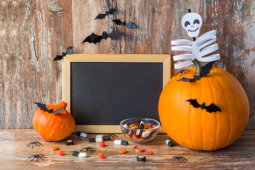 holidays, school and party concept - halloween pumpkins, decorations with blank chalkboard on wooden boards background