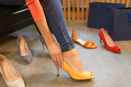 sale, shopping, fashion and people concept - young woman choosing high-heeled peep toe shoes at store