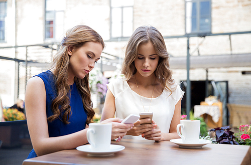 technology, lifestyle, internet addiction and people concept - young women with smartphones drinking coffee at cafe outdoors