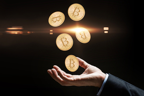 cryptocurrency, finance and business concept - close up of businessman hand with bitcoins over black background