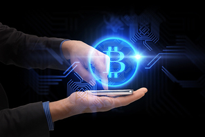 business, cryptocurrency and future technology concept - close up of male hands holding smartphone with virtual bitcoin symbol hologram over black background