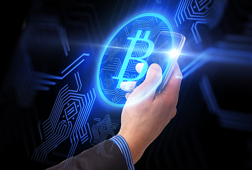 business, cryptocurrency and future technology concept - close up of male hand holding smartphone with virtual bitcoin symbol hologram over black background