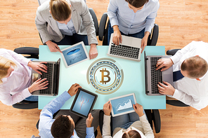 cryptocurrency, technology and finance concept - close up of business team with laptops, tablet pc computers and bitcoin hologram sitting at office table from top