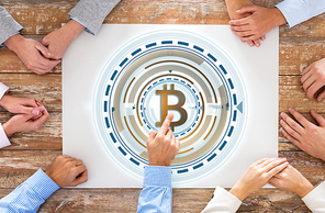 business, cryptocurrency and finance concept - close up of team sitting at wooden table with bitcoin hologram at office from top
