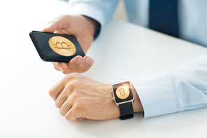 business, technology and cryptocurrency concept - close up of male hand holding smartphone and wearing smart watch with bitcoin on screen