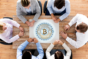 business, cryptocurrency and finance concept -team sitting at wooden table with bitcoin hologram in office, shot from top