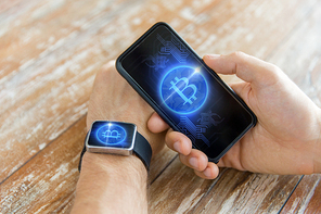 business, technology and cryptocurrency concept - close up of male hand holding smartphone and wearing smart watch with bitcoin on screen