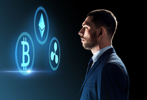 cryptocurrency, financial technology and business concept - buisnessman looking at virtual bitcoin, ethereum and ripple icons over dark background