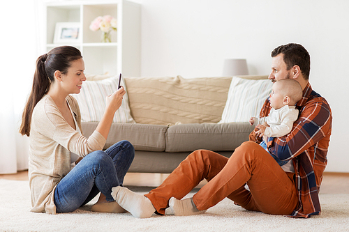 family, parenthood and people concept - happy mother with smartphone taking picture of father with baby at home