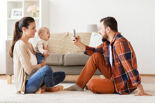 family, parenthood and people concept - happy father with smartphone taking picture of mother with baby at home