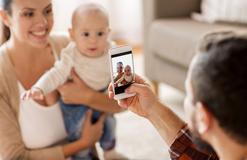 family, parenthood and people concept - happy father with smartphone taking picture of mother with baby at home