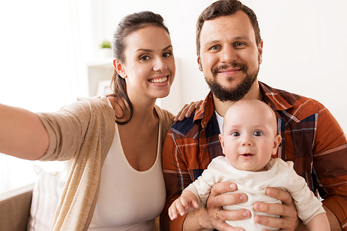 family, parenthood and people concept - happy mother and father with baby taking selfie at home