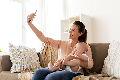 family, technology, motherhood and people concept - happy mother with little baby boy taking selfie at home