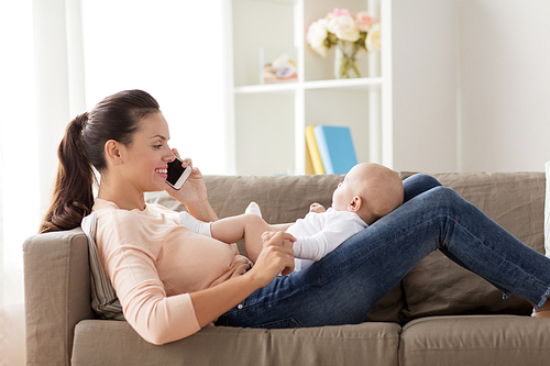 family, technology, motherhood and people concept - happy mother with little baby boy lying on sofa and calling on smartphone at home