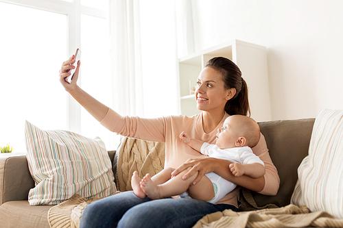 family, technology, motherhood and people concept - happy mother with little baby boy taking selfie at home