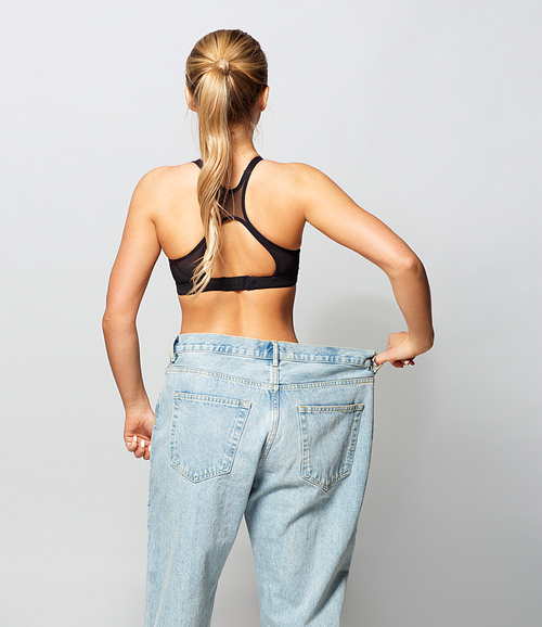 fitness, diet, weight loss and people concept - young slim sporty woman in oversize pants
