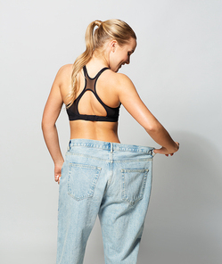 fitness, diet, weight loss and people concept - young slim sporty woman in oversize pants