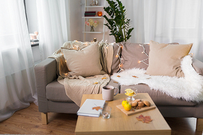 comfort, hygge, cozy home and interior concept - sofa with cushions and garland lights in living room