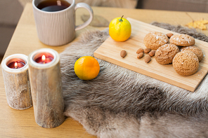 hygge and cozy home concept - oatmeal cookies, lemon tea and candles on wooden table in living room