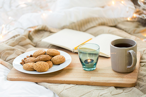 food, hygge and comfort concept - oatmeal cookies, tea, diary and candle in holder at home