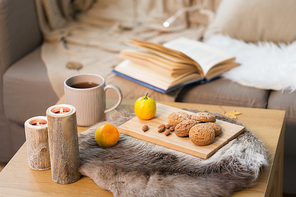 hygge and cozy home concept - oatmeal cookies, lemon tea and candles on wooden table in living room