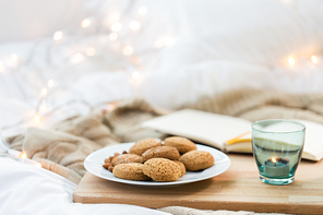 food, bakery and hygge concept - oatmeal cookies on plate and candle in holder at home