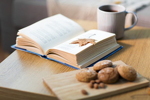 hygge and cozy home concept - book with autumn leaf, cup of tea and oatmeal cookies on wooden table