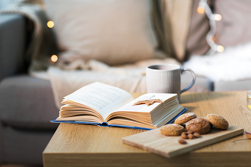 hygge and cozy home concept - book with autumn leaf, cup of tea and oatmeal cookies on wooden table