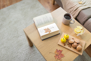 hygge and cozy home concept - book, autumn leaves, cup of tea with lemon, almond nuts and oatmeal cookies on table