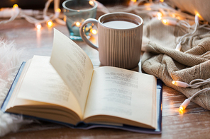 hygge and cozy home concept - book and cup of coffee or hot chocolate on table