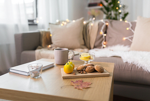 hygge and cozy home concept - oatmeal cookies, book, tea and lemon on wooden table in living room