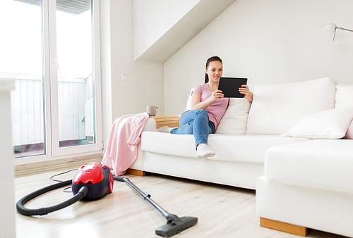 cleaning, household and technology concept - happy woman or housewife with tablet pc computer and vacuum cleaner at home